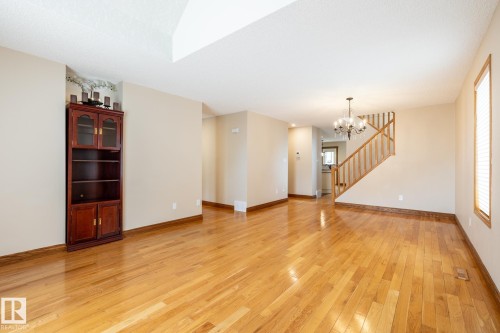 Expansive living area featuring wood-finish flooring, a chandelier, a staircase with wood railings, a window with blinds, and neutral wall tones - 4632 151 Street, Edmonton, AB - Indoor Photo Showing Other Room