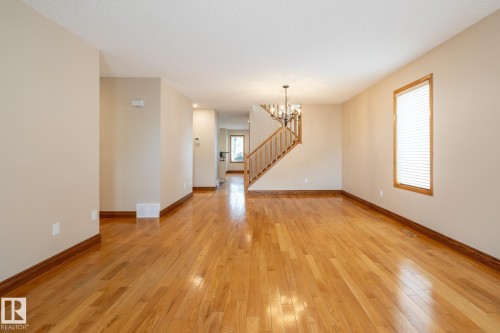 Spacious interior featuring wood-finish flooring, light neutral wall paint, and a staircase with wood banisters - 4632 151 Street, Edmonton, AB - Indoor Photo Showing Other Room