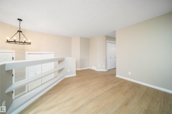 Open loft area featuring wood-finish flooring, a contemporary chandelier with a matte black finish, and light neutral wall paint - 