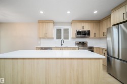 Kitchen featuring a spacious island with a white countertop, light wood-finish cabinetry, stainless steel appliances, and recessed lighting - 