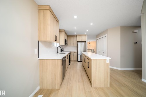 Modern kitchen featuring wood-finish cabinetry, stainless steel appliances, a center island with a white countertop, recessed lighting, and wood-finish flooring - 1212 Ormsby Lane, Edmonton, AB - Indoor Photo Showing Kitchen