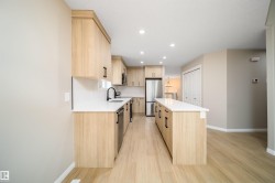 Modern kitchen featuring wood-finish cabinetry, stainless steel appliances, a center island with a white countertop, recessed lighting, and wood-finish flooring - 