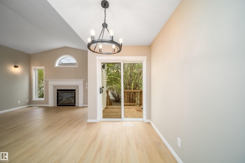 Vaulted ceiling room featuring light wood-finish flooring, a tiled fireplace with mantel, and a half-round transom window - 1212 Ormsby Lane, Edmonton, AB - Indoor With Fireplace