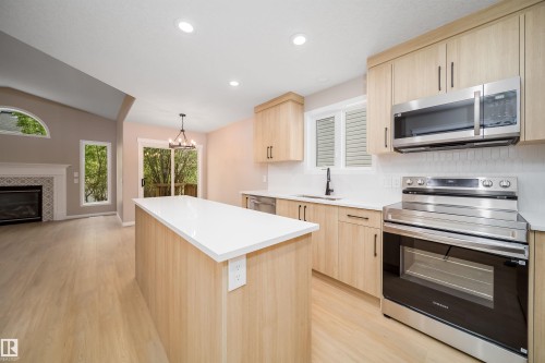 Kitchen featuring a center island with a white countertop, light wood-finish cabinetry, stainless steel appliances, and a white geometric tile backsplash - 1212 Ormsby Lane, Edmonton, AB - Indoor Photo Showing Kitchen