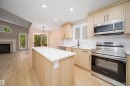 Kitchen featuring a center island with a white countertop, light wood-finish cabinetry, stainless steel appliances, and a white geometric tile backsplash - 1212 Ormsby Lane, Edmonton, AB  - Indoor Photo Showing Kitchen 