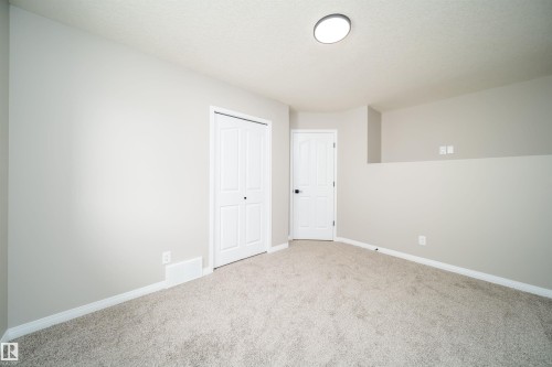 Interior room featuring light gray wall paint, light-colored carpet flooring, a white bi-fold closet door, a white interior door with black hardware, and a ceiling-mounted light fixture - 1212 Ormsby Lane, Edmonton, AB - Indoor Photo Showing Other Room