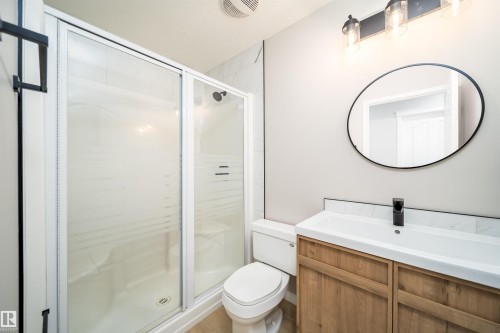 Contemporary bathroom featuring a wood-finish vanity with an integrated sink, matte black faucet, and oval mirror - 1212 Ormsby Lane, Edmonton, AB - Indoor Photo Showing Bathroom