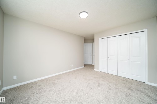 Spacious room featuring light-colored carpeting, neutral wall tones, white baseboards, and a large bi-fold closet with panel doors - 1212 Ormsby Lane, Edmonton, AB - Indoor Photo Showing Other Room
