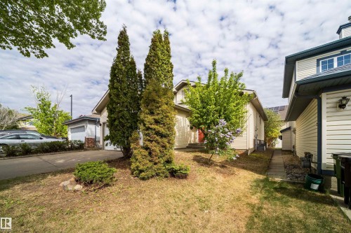 Front exterior featuring light-colored siding, a dark blue trim, a red front door, and a paved driveway - 1212 Ormsby Lane, Edmonton, AB - Outdoor