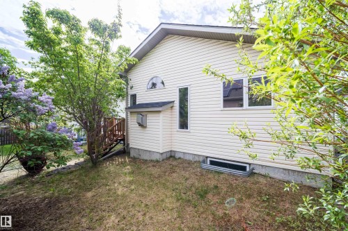 Light-toned siding exterior featuring a prominent arched window, multiple rectangular windows, and a basement window well - 1212 Ormsby Lane, Edmonton, AB - Outdoor With Exterior