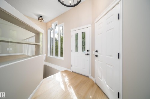 Foyer featuring wood-finish flooring, a white paneled entry door with decorative glass inserts, and a coordinating white interior door with black hardware - 1212 Ormsby Lane, Edmonton, AB - Indoor Photo Showing Other Room