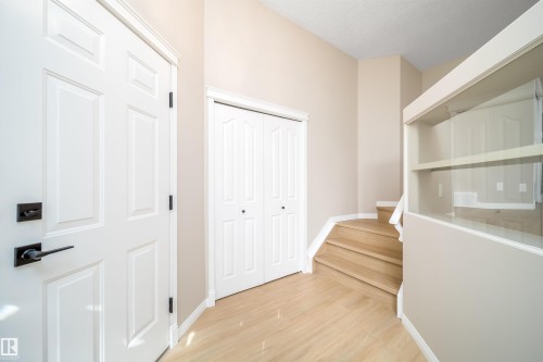 Entryway featuring light wood-finish flooring, a six-panel door with matte black hardware, a bi-fold closet door, and a staircase with wood treads and a white railing - 1212 Ormsby Lane, Edmonton, AB - Indoor Photo Showing Other Room