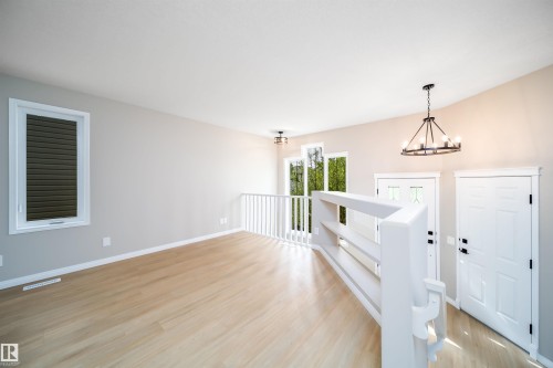 Spacious interior featuring wood-finish flooring, a white railing system, and a contemporary black chandelier - 1212 Ormsby Lane, Edmonton, AB - Indoor Photo Showing Other Room