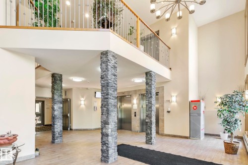 Two-story foyer featuring stone-clad columns, two stainless steel elevators, and wood-finish flooring - 334 10121 80 Avenue, Edmonton, AB - Indoor Photo Showing Other Room