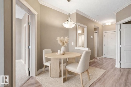 Dining area featuring wood-finish flooring, crown molding, and a contemporary pendant light fixture - 334 10121 80 Avenue, Edmonton, AB - Indoor Photo Showing Dining Room
