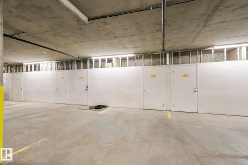 A row of storage units with white doors and numerical labels, set against a concrete wall - 334 10121 80 Avenue, Edmonton, AB - Indoor Photo Showing Garage