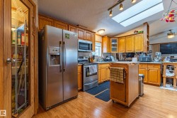 Kitchen featuring wood-finish flooring, ample wood cabinetry, stainless steel appliances, and a skylight - 