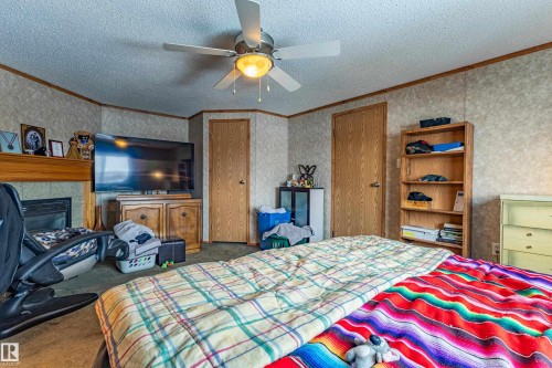 Interior space featuring a ceiling fan with integrated lighting, wood-finish doors, textured wall paneling, and a built-in fireplace with a wood mantle - 1529 Range Road 272 Rural Parkland County, Alberta, Rural Parkland County, AB - Indoor Photo Showing Bedroom