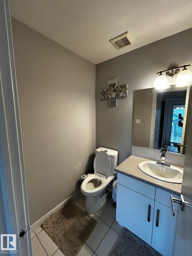 Bathroom featuring white square tile flooring, a white vanity with a light-colored countertop, and a vanity light fixture - 1868 30 Street Nw, Edmonton, AB - Indoor Photo Showing Bathroom