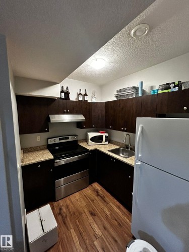 Compact kitchen featuring wood-finish flooring, dark cabinetry, and speckled countertops - 1868 30 Street Nw, Edmonton, AB - Indoor Photo Showing Kitchen