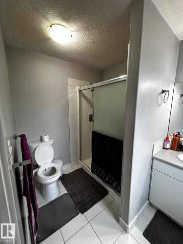 Three-quarter bathroom featuring a shower with a sliding glass door, a toilet, and a single vanity with a laminate countertop - 1868 30 Street Nw, Edmonton, AB - Indoor Photo Showing Bathroom