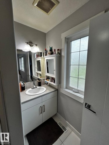 Compact bathroom featuring a single vanity with an oval sink, a light-toned countertop, and white cabinetry - 1868 30 Street Nw, Edmonton, AB - Indoor Photo Showing Bathroom