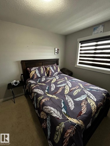 Carpeted flooring, window with horizontal blinds, wall-mounted light fixture, and dark wood-finish headboard - 1868 30 Street Nw, Edmonton, AB - Indoor Photo Showing Bedroom