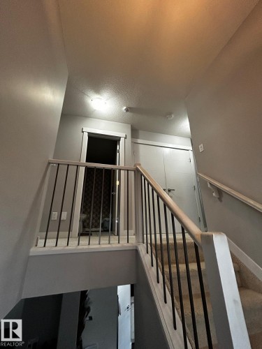 Carpeted staircase with light wood-finish railings and black metal balusters - 1868 30 Street Nw, Edmonton, AB - Indoor Photo Showing Other Room