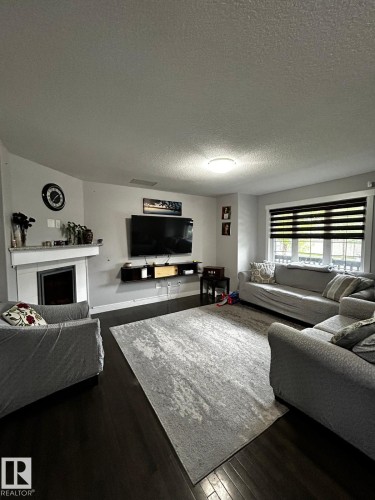 Living area featuring dark wood-finish flooring, a white mantel fireplace, and a large window with horizontal blinds - 1868 30 Street Nw, Edmonton, AB - Indoor Photo Showing Living Room
