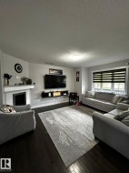 Living area featuring dark wood-finish flooring, a white mantel fireplace, and a large window with horizontal blinds - 