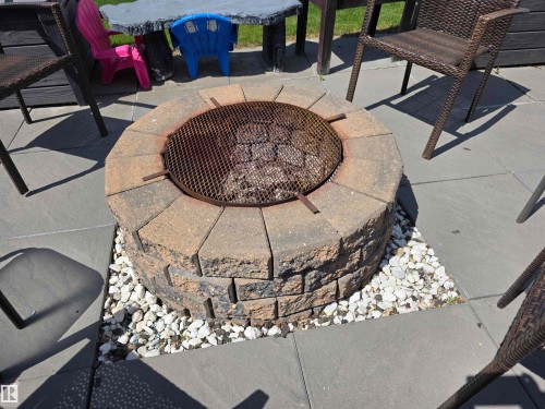 Circular stone paver fire pit with a metal grate, surrounded by white decorative gravel and gray patio pavers - 5012 53 Ave, Breton, AB 