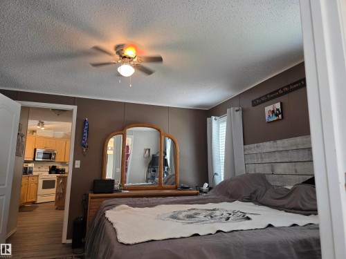 Room featuring a ceiling fan with integrated lighting, wood-finish flooring, a white window blind, and a decorative paneled wall accent - 5012 53 Ave, Breton, AB 