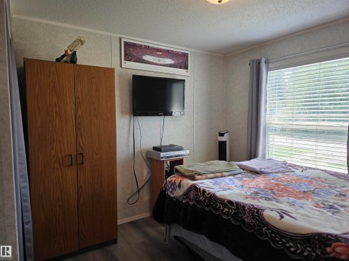 Bedroom featuring a large window with blinds, wood-finish flooring, and a ceiling light fixture - 5012 53 Ave, Breton, AB 