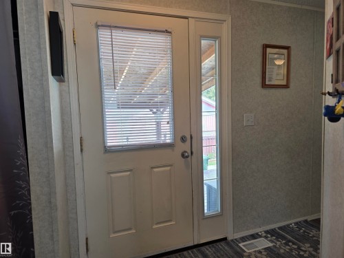 Entryway featuring a paneled door with integrated blinds, a full-length sidelight, textured wall panels, and patterned flooring - 5012 53 Ave, Breton, AB 