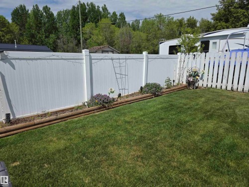 Manicured lawn with a white vinyl privacy fence and a white picket fence - 5012 53 Ave, Breton, AB 