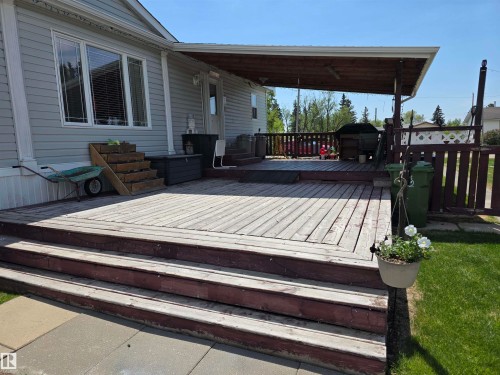Expansive wood deck with two-tier steps, partial overhead covering, and perimeter wood fencing - 5012 53 Ave, Breton, AB 