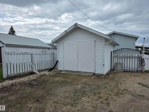 Detached garage with white siding and pitched roof, featuring double panel doors and an exterior side door - 5012 53 Ave, Breton, AB 