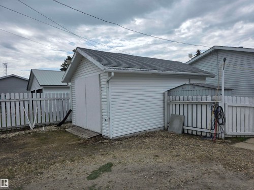 Detached garage with white vinyl siding, a gray shingle roof, and dual wooden swing-out doors - 5012 53 Ave, Breton, AB 