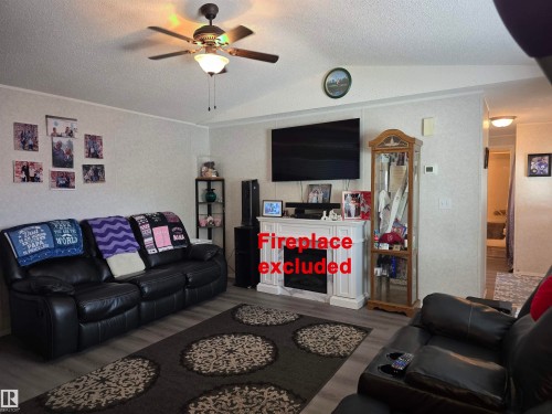 Living area featuring wood-finish flooring, a ceiling fan with integrated lighting, and textured wall coverings - 5012 53 Ave, Breton, AB 