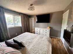 Spacious room featuring wood-finish flooring, a contemporary ceiling light fixture, and a large window with privacy drapes. - 