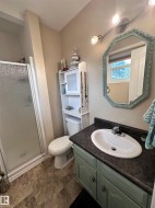 Featuring a vanity with a drop-in sink, a track light fixture, an octagonal mirror, a shower enclosure with a frosted glass door, and vinyl flooring - 