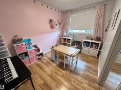 Bright interior space featuring wood-finish flooring, a large window with roller shade, and built-in shelving. - 