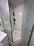 White shower enclosure with glass doors and chrome hardware, featuring a built-in shelf and a shower head. - 