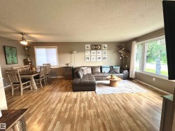 Spacious living and dining area featuring wood-finish flooring, a ceiling fan, and large windows. - 