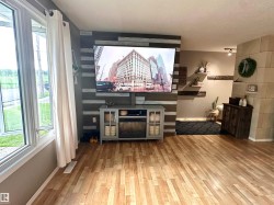 Hardwood flooring throughout a spacious room featuring a window with white trim, a decorative accent wall with horizontal wood planks. - 