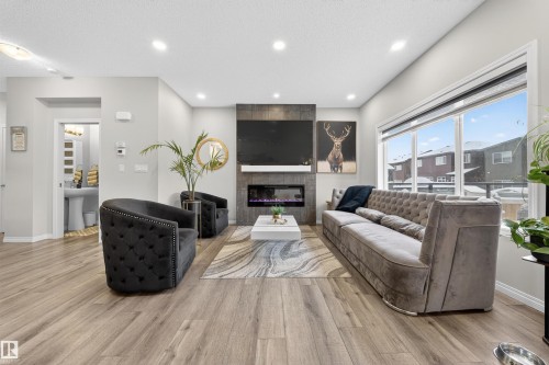 Spacious living area featuring large windows, wood-finish flooring, recessed lighting, and a modern fireplace with a dark-toned surround - 6085 King Landing, Edmonton, AB - Indoor Photo Showing Living Room With Fireplace