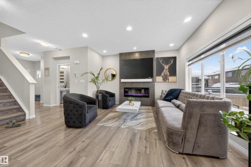 Open-concept living space featuring wood-finish flooring, recessed lighting, and a linear electric fireplace with stone-look surround - 6085 King Landing, Edmonton, AB - Indoor Photo Showing Other Room With Fireplace