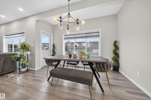 Dining space featuring a linear chandelier with exposed bulbs, wood-finish flooring, two large windows, a white panel door, and recessed lighting - 6085 King Landing, Edmonton, AB - Indoor