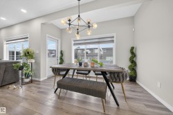 Dining space featuring a linear chandelier with exposed bulbs, wood-finish flooring, two large windows, a white panel door, and recessed lighting - 