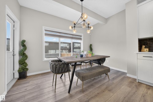 Spacious dining area featuring wood-finish flooring, a contemporary chandelier, large window with natural light, a white exterior door, and built-in cabinetry with a dark tile backsplash - 6085 King Landing, Edmonton, AB - Indoor Photo Showing Dining Room